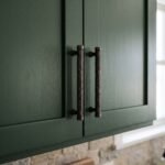 Dos columnas de volutas en puerta verde de cocina en bronce envejecido